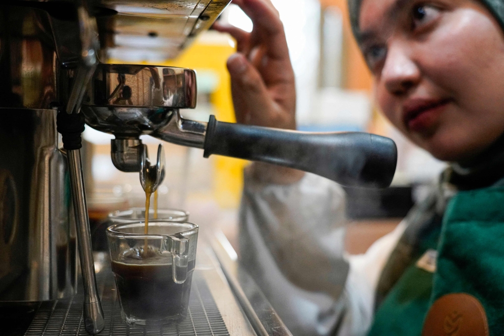 Morning Mama owner Qurrata Ayuni, who lost her parents in the 2004 tsunami, makes a coffee at her cafe in Banda Aceh. — AFP pic