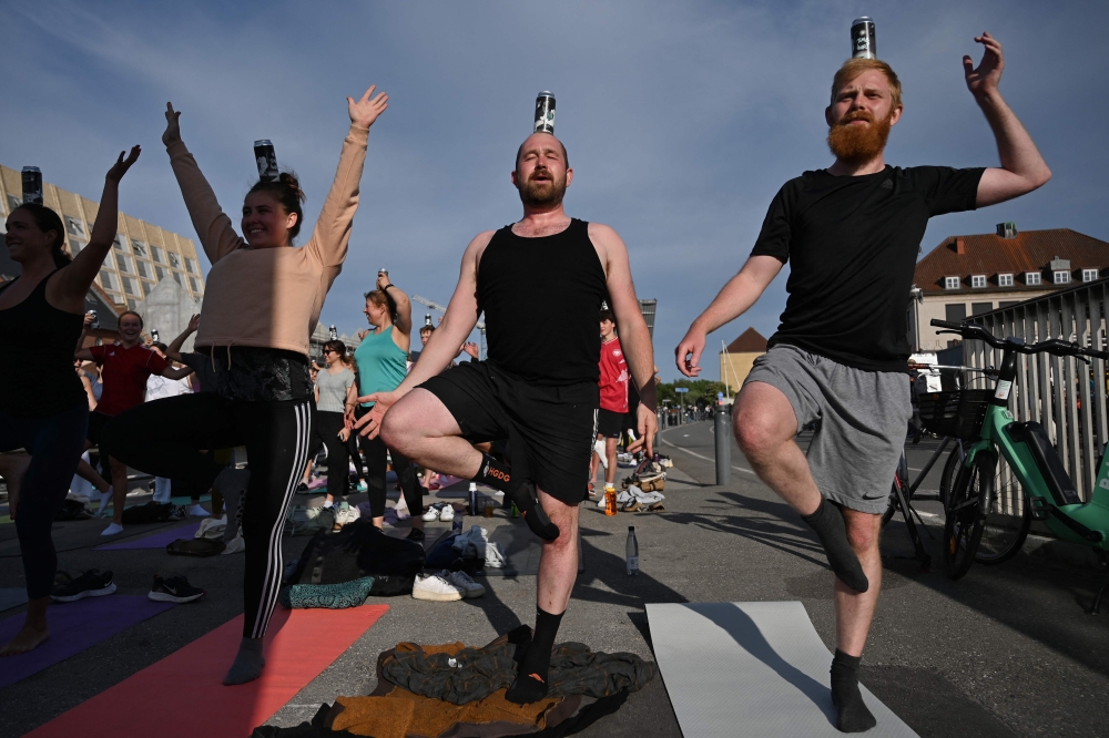 People balance a can of beer as they attend the so-called ‘Beer Yoga event’ in Copenhagen, on May 31, 2023. — AFP pic 