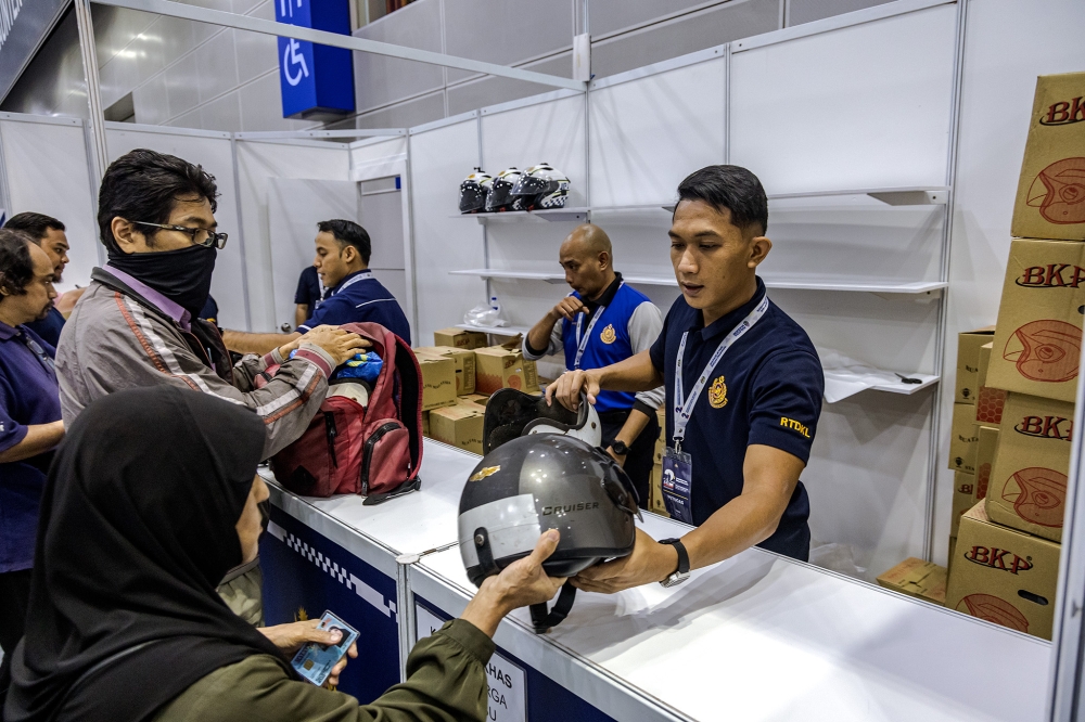 A Road Transport Department staff member hands out helmets at the Helmet Exchange Program during the Madani Government's two-year anniversary event at the Kuala Lumpur Convention Centre on November 22. 2024. — Picture by Firdaus Latif