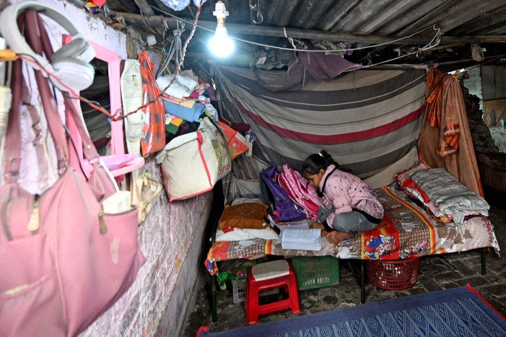 Harshita Gautam attends an online class on a mobile phone in her shanty in New Delhi on November 22, 2024. — AFP pic