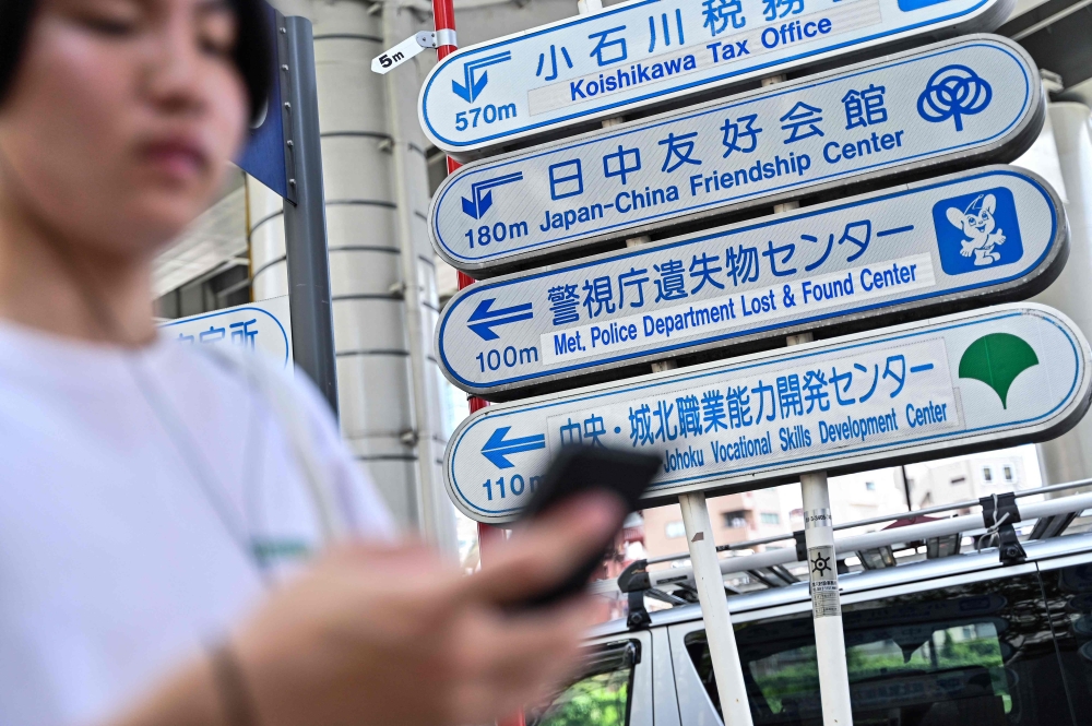 A pedestrian walks past a signboard giving directions (3rd down) for the nearby Tokyo Metropolitan Police Department Lost and Found Centre in the Iidabashi area of central Tokyo August 2, 2024. — AFP pic