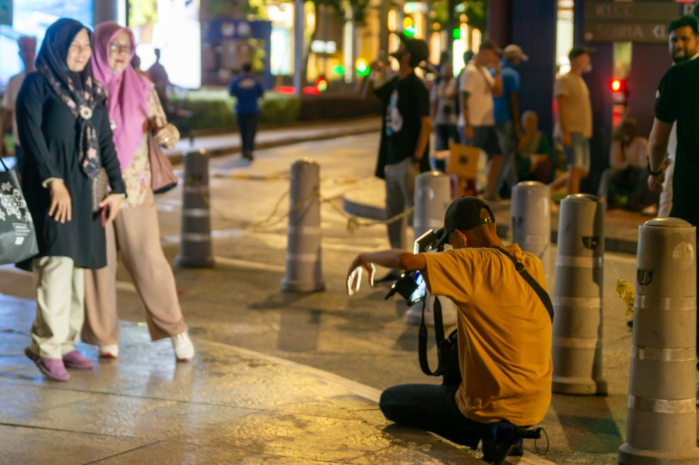 A street photo tout captures a moment for a visitor near KLCC, Kuala Lumpur. — Picture by Raymond Manuel