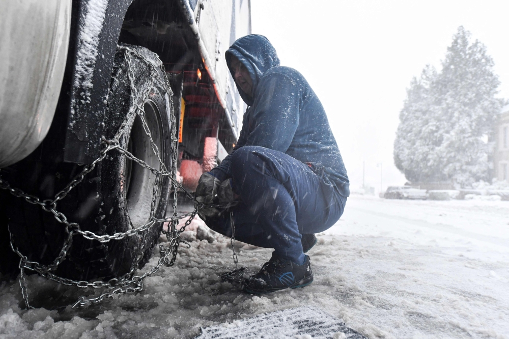 A truck driver puts chains on the wheels of his truck in Beaumont-les-Autels, central France, on November 21, 2024 as the first flakes of storm Caetano fell in France. — AFP pic