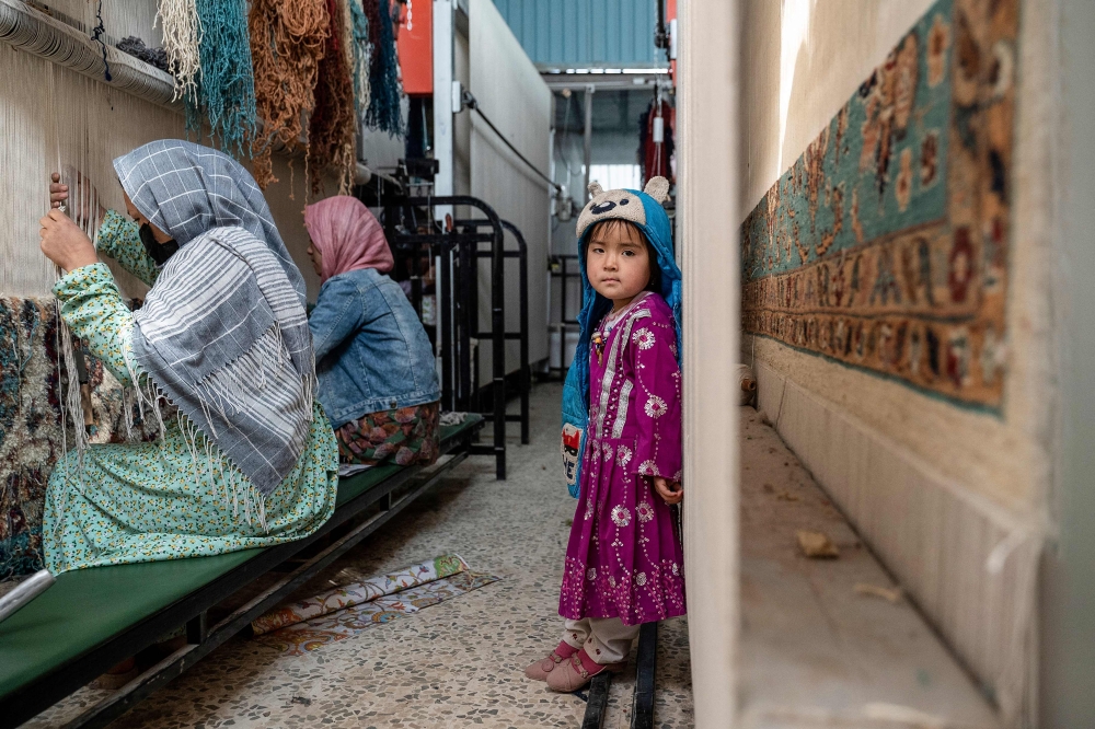 An Afghan girl looks on as women weave carpets at a factory on the outskirts of Kabul. — AFP pic