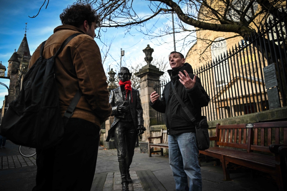 Invisible Cities guide Sonny Murray leads a walking tour with student Arthur Lyhne-Gold, in front of Cannongate Kirk, Edinburgh, November 17, 2024. — AFP pic