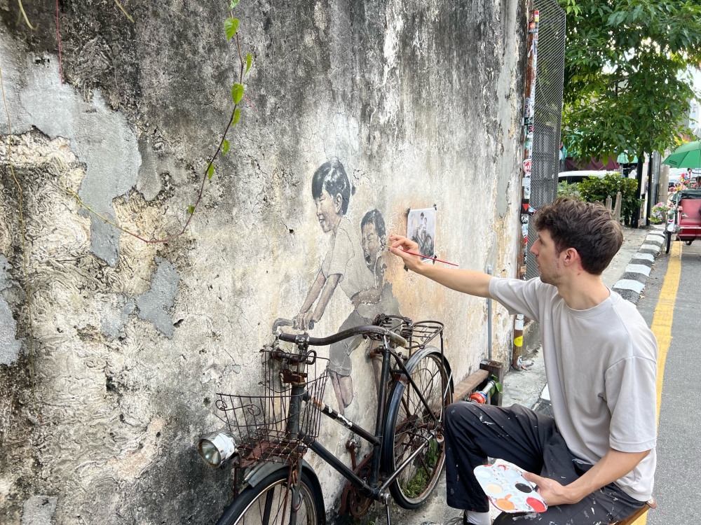 Ernest Zacharevic restoring 'Children on Bicycle' street art at Armenian Street based on a photo taken of the mural when it was first completed in 2012. — Picture by Opalyn Mok