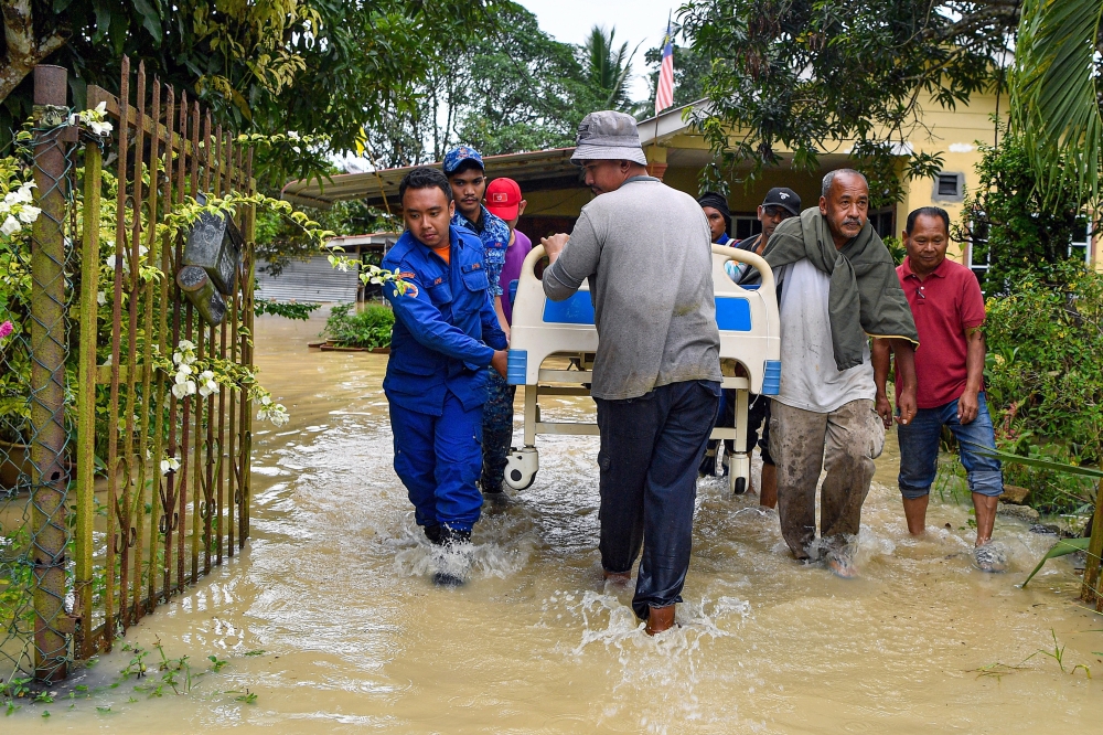 Members of the Malaysian Civil Defense Force join hands with villagers to lift a bed with a patient, who was also a flood victim, to be placed at the SK Londah temporary relief centre in Tampin November 29, 2024. — Bernama pic