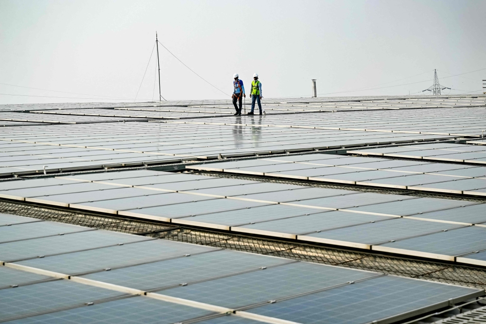 This photograph taken on November 21, 2024 shows employees at SunSource Energy inspecting solar panels installed at a food processing plant of the Indian food service company Jubilant FoodWorks in Greater Noida. India vows to be carbon neutral by 2070 and as part of that, New Delhi wants its renewable energy capacity to rise from 200 GW — half of its current energy mix — to 500 GW by 2030. It hopes 300 GW will come from solar power alone. — AFP pic