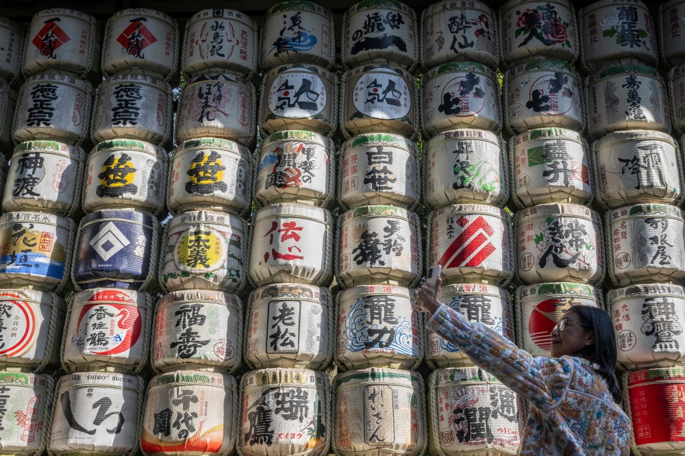 A woman takes selfies in front of a display of sake barrels at Meiji Shrine in Tokyo on December 5, 2024. — AFP pic