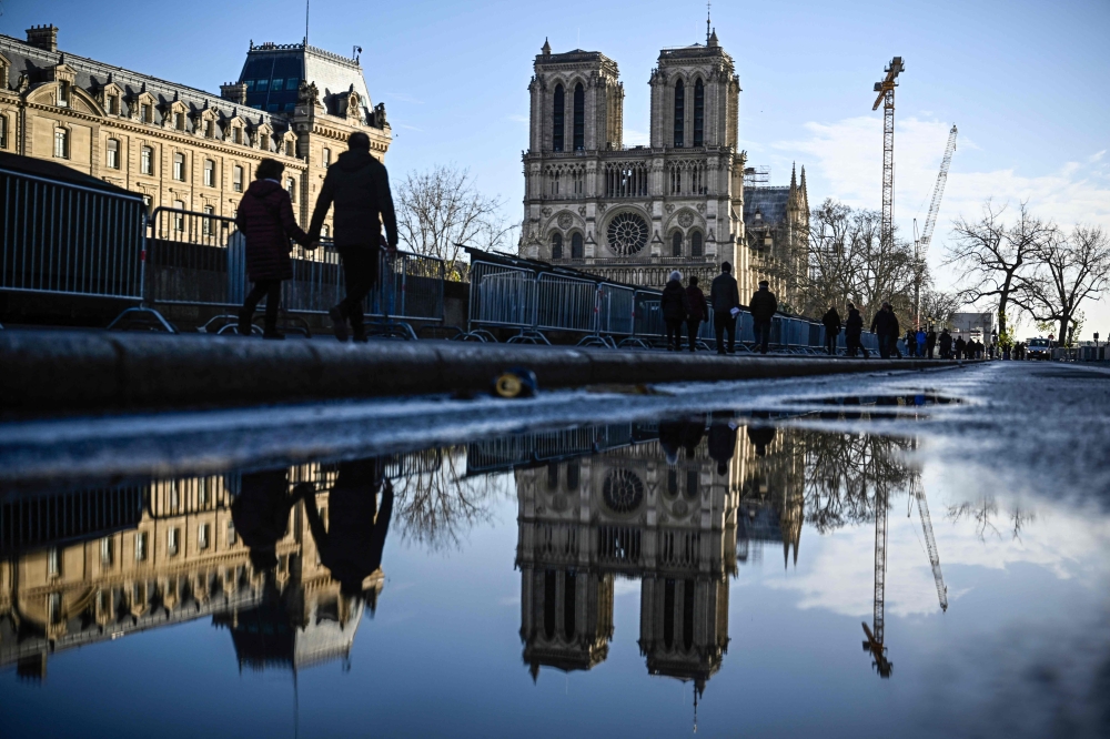 Pedestrians pass by the security barriers and fences placed around the Notre-Dame de Paris cathedral on the eve ahead of its official reopening after more than five-year of reconstruction work following the April 15, 2019 fire, in Paris, on December 6, 2024. — AFP pic