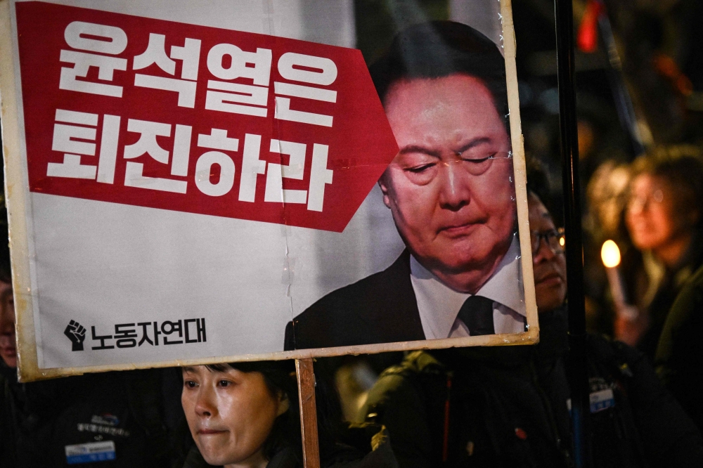 A woman holds a sign that reads ‘Yoon Suk Yeol should step down’ during a candlelight vigil against South Korea President Yoon in Seoul on December 4, 2024. South Korea’s opposition moved to impeach Yoon on December 4 after his extraordinary but short-lived imposition of martial law that brought thousands of protesters to the streets. — AFP pic