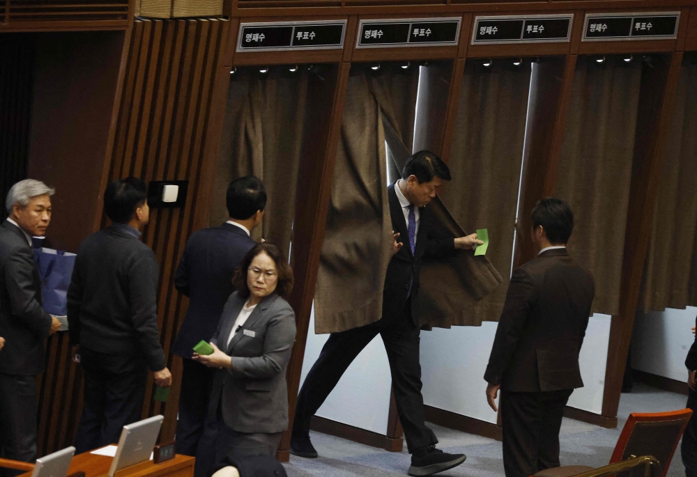 Lawmakers queue to cast their votes in polling booths on proposed legislation for appointing a special prosecutor to investigate allegations of stock price manipulation involving the president's wife during a plenary session for the impeachment vote of President Yoon Suk Yeol at the National Assembly in Seoul on December 7, 2024. — Jeon Heon-kyun/Pool/AFP pic 