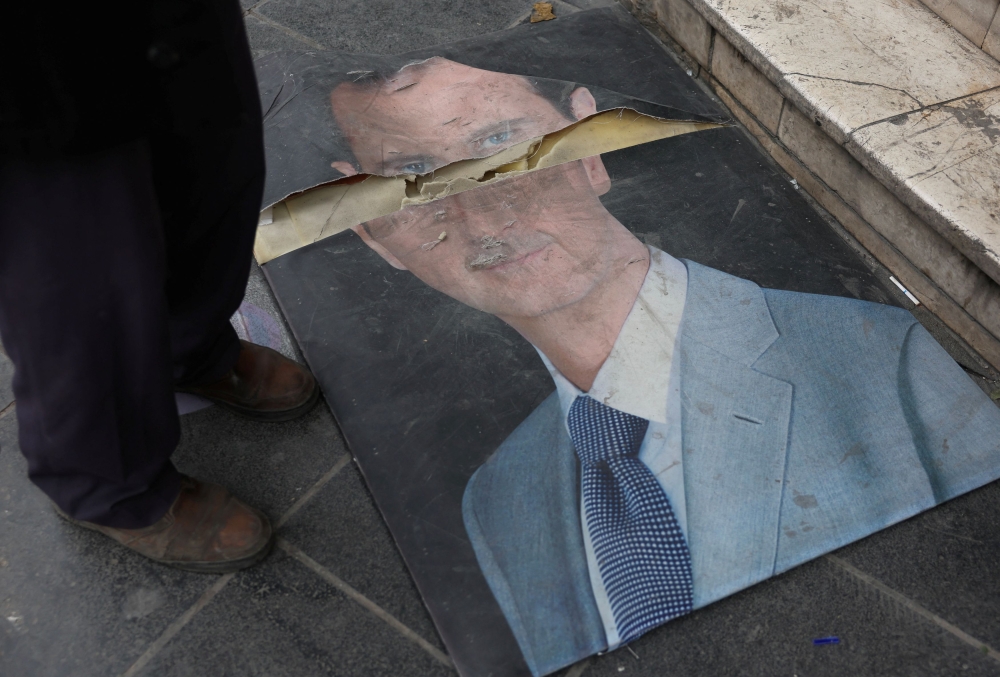 A person stands next to a damaged picture of Syria's Bashar al-Assad in Damascus, after rebels seized the capital and ousted him, Syria December 11, 2024. — Reuters pic  