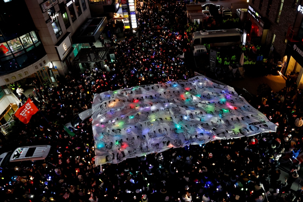 Protesters hold a banner depicting faces of ruling People Power Party lawmakers during in a rally calling for the impeachment of South Korean President Yoon Suk Yeol, who declared martial law, which was reversed hours later, in front of the headquarters of the ruling People Power Party, in Seoul, South Korea, December 12, 2024. — Reuters pic