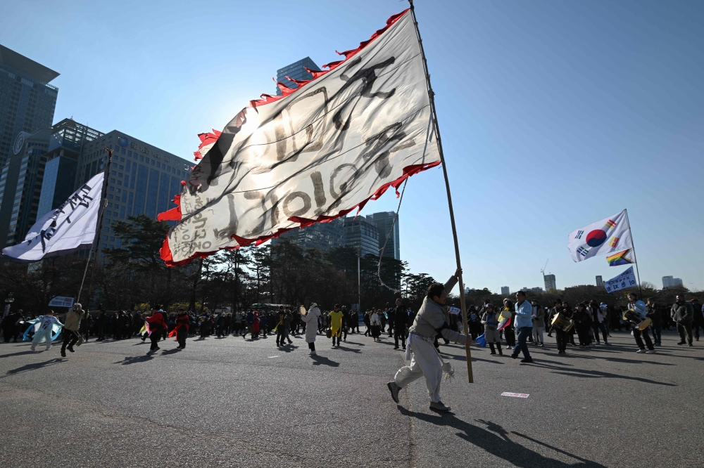 A man holds a flag reading ‘The people are the rulers’ during a protest calling for the ouster of South Korea’s President Yoon Suk Yeol outside the National Assembly in Seoul December 14, 2024. — AFP pic