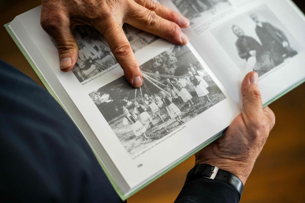 Michael Lisske points with his finger on an old photograph showing his wife, Carmen Schuster, as a young local girl taking part in a celebration in Cincsor, a small Transylvanian village some 250km north-west of Bucharest October 17, 2024. — AFP pic