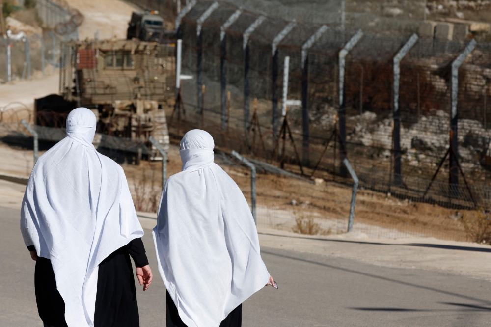 Druze women walk near the fence leading into the UN-patrolled buffer zone, which separates Israeli and Syrian forces on the Golan Heights, near the Druze village of Majdal Shams in the Israel-annexed Golan Heights on December 15, 2024. — AFP pic