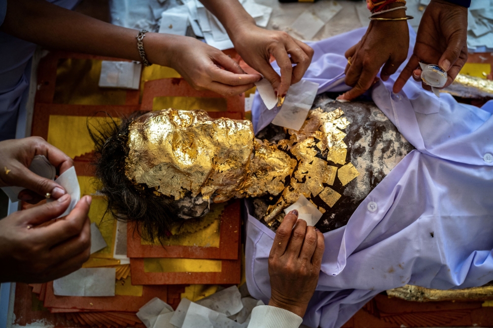 A preserved body is adorned with gold leaf by volunteers. — Reuters