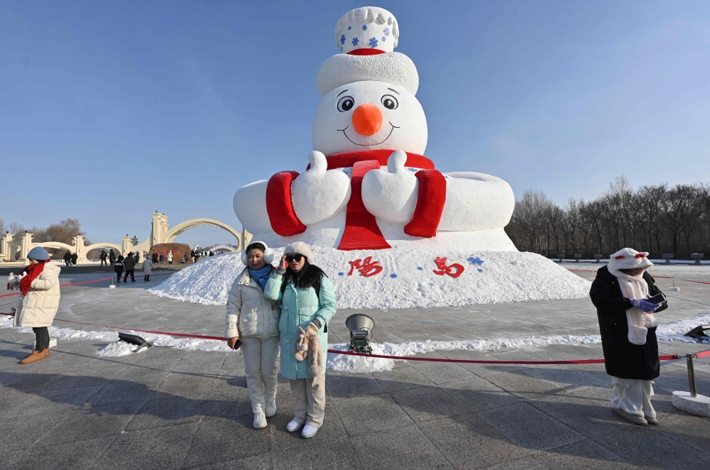 Visitors pose for pictures with a snowman sculpture ahead of the annual Harbin Ice and Snow World Festival December 17, 2024. — AFP pic