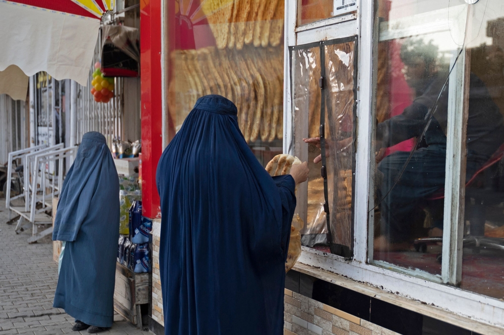 An Afghan burqa-clad woman buys traditional flatbreads locally known as Naan, from a roadside bakery in Kabul November 27, 2024. — AFP pic