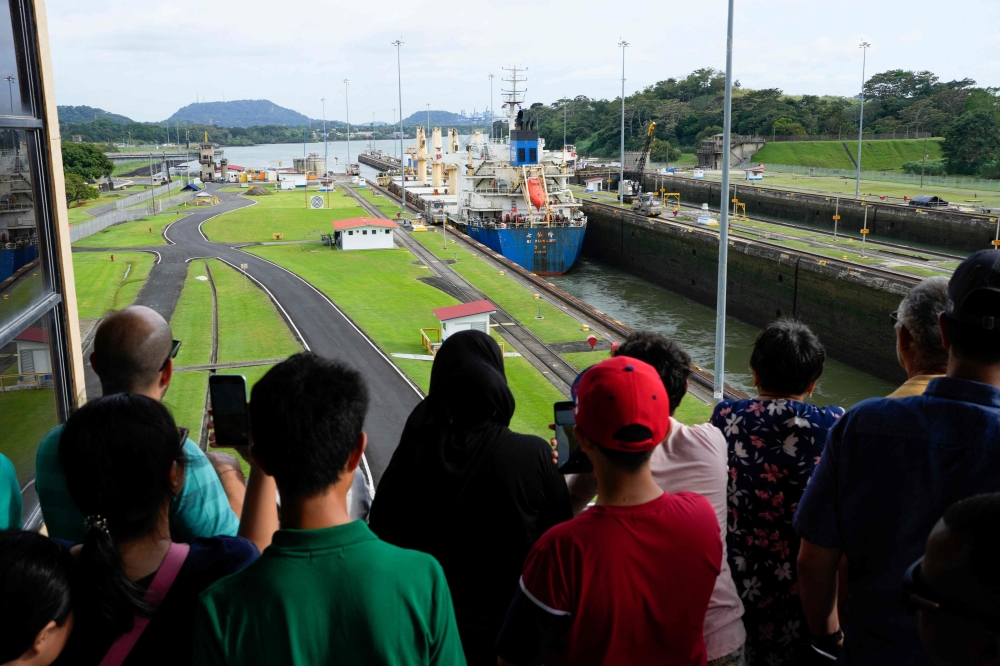 Tourists watch a cargo ship transit through the Panama Canal in Panama City on December 23, 2024. — AFP pic