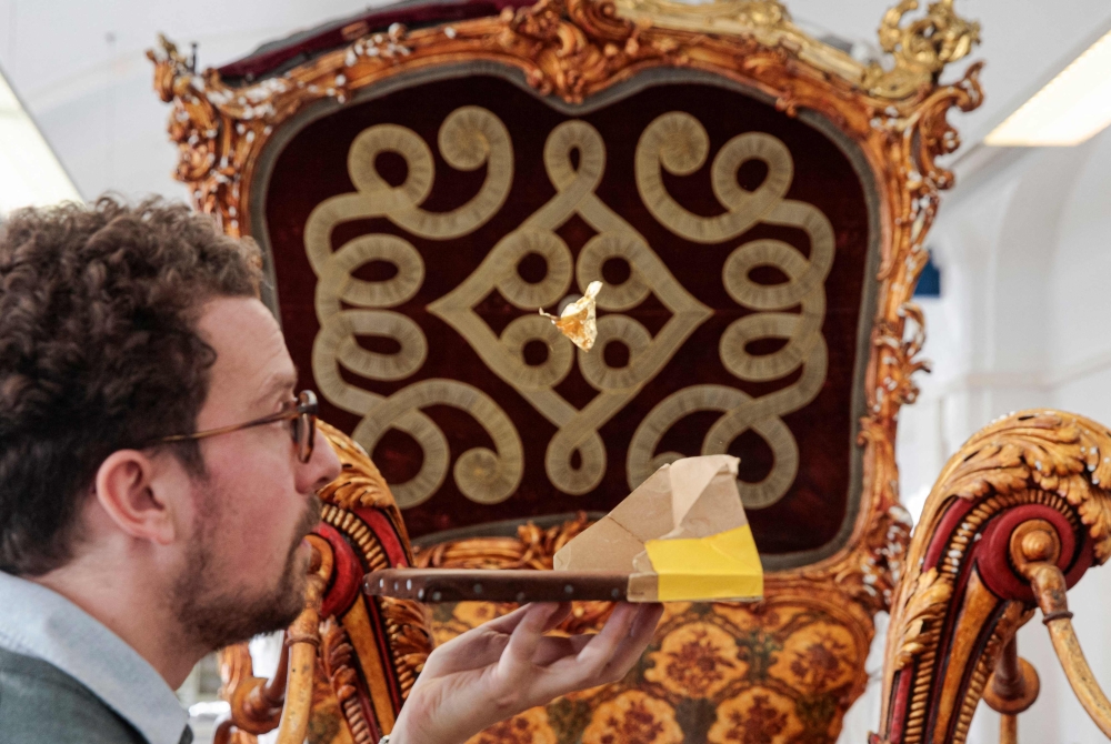 Museum's conservator Matthias Mazini gently blows a piece of gold leaf into the air while restoring a carriage, in the studio of the Kunsthistorisches Museum (KHM) in Vienna on December 5, 2024. — AFP pic