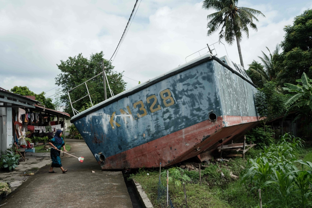 Syafriani, 41, whose mother is still missing after the 2004 Indian Ocean tsunami, cleans in front of her house where two patrol boats washed ashore and remain preserved at the community's wish, in Banda Aceh on December 25, 2024. — AFP pic