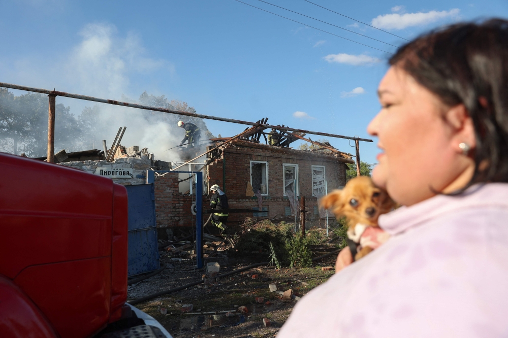 Bakhmut resident Anna Holubtsova watches as firefighters extinguish a fire in a private house damaged by shelling in Bakhmut, Donetsk region, on October 8, 2022, amid the Russian invasion in Ukraine. — AFP pic