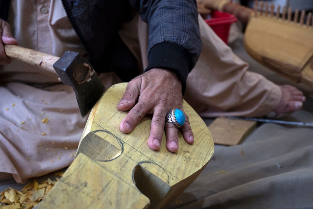 Afghan craftsman Sakhi uses a hatchet as he makes a rubab, a string instrument of dried mulberry wood from deserts, at a workshop in Herat December 22, 2024. — AFP pic