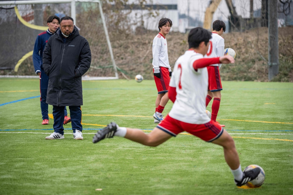 Masahiro Enomoto (left), manager of Ryutsukeizai University Kashiwa High School football club, looks on during a training session at their school football field in Kashiwa city of Chiba prefecture December 13, 2024. — AFP pic