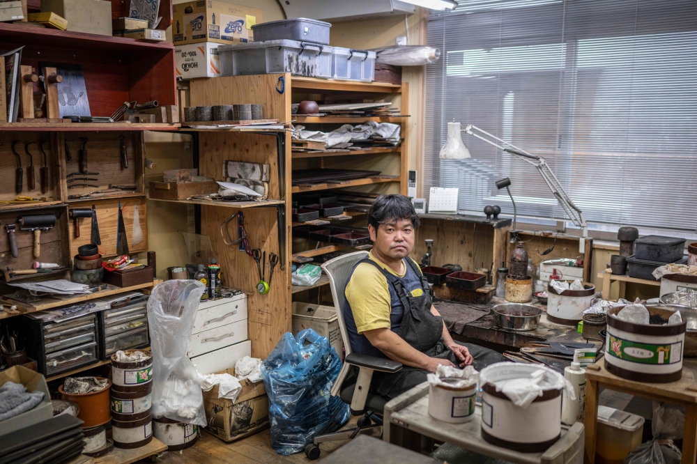 Japanese lacquerware maker Takaho Shoji poses for photographs at his desk in the Wajima Kirimoto lacquerware studio in Wajima city, Ishikawa prefecture, December 11, 2024. — AFP pic