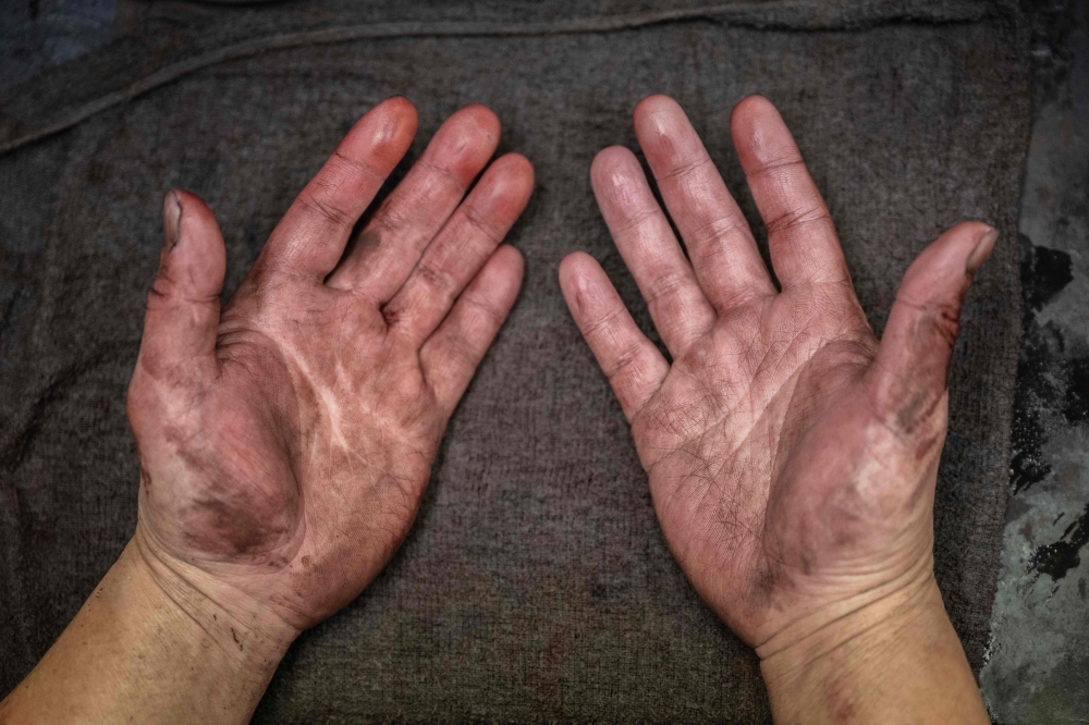 Japanese lacquerware maker Takaho Shoji shows his hands at his desk in the Wajima Kirimoto lacquerware studio in Wajima city, Ishikawa prefecture December 11, 2024. — AFP pic