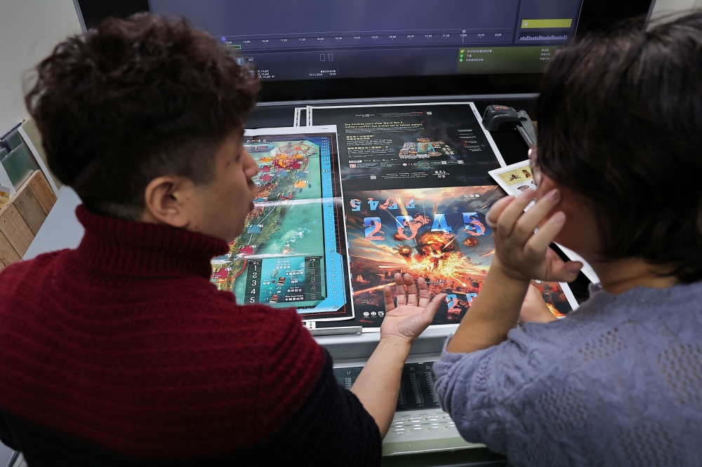 Chang Shao Lian, the founder of Mizo Games, discusses and checks the printing of ‘2045’, a new board game set against the backdrop of armed conflicts around Taiwan, in New Taipei City December 10, 2024. — Reuters pic  