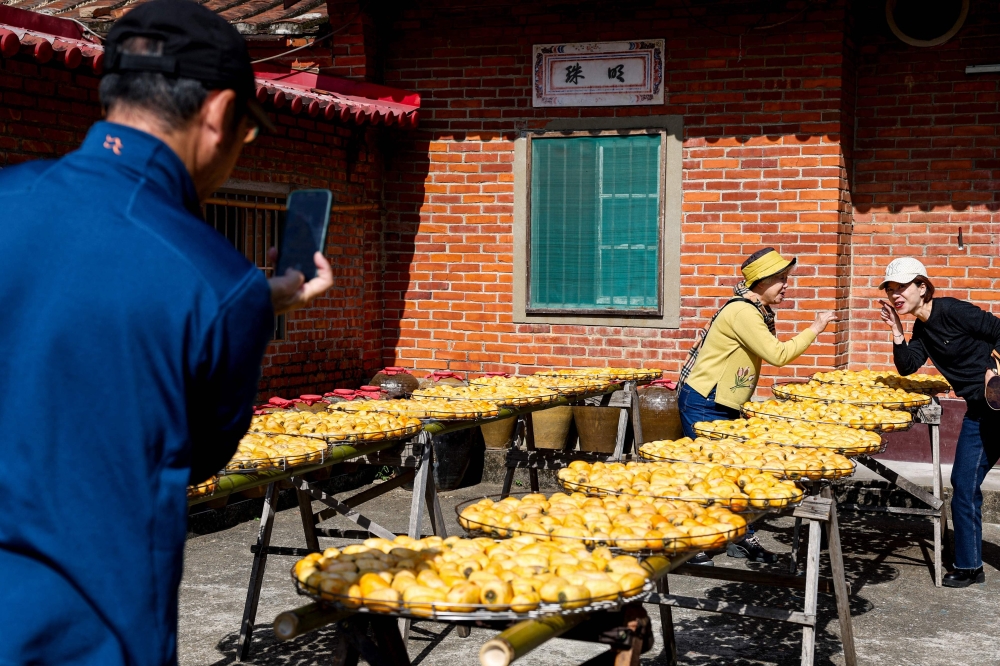 Tourists take pictures with dried persimmons at Weiweijia persimmon farm in Xinpu township, Hsinchu county on December 17, 2024. — AFP pic