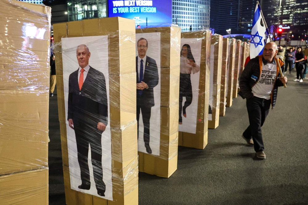 A protester walks past of images of Israeli polititians depicted as dominoes during a demonstration calling for the release of hostage. — AFP