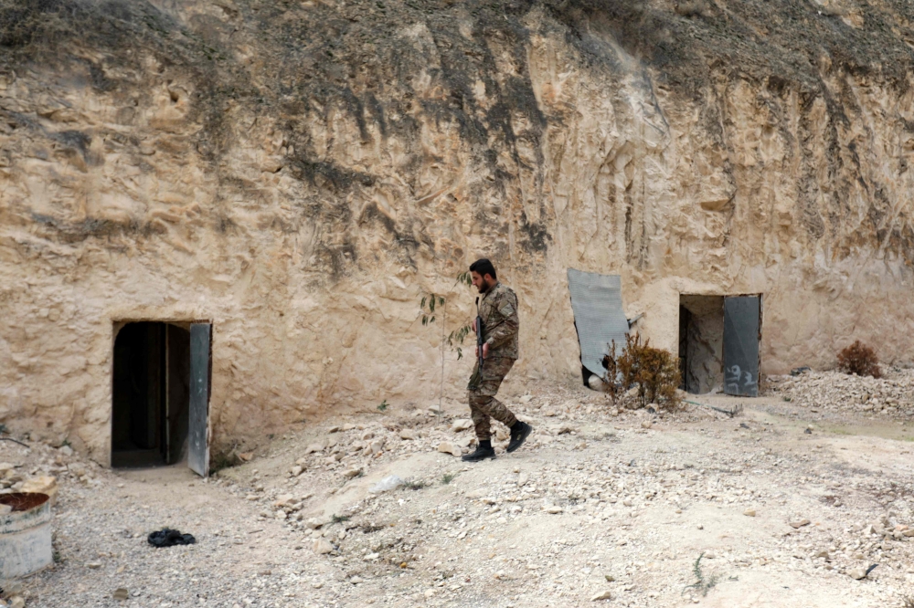 A fighter affiliated with Syria's new administration walks along a cliff with entrances leading to tunnels, inside the abandoned Syrian Republican Guard (SRG) base near Damascus on January 4, 2025. — AFP pic