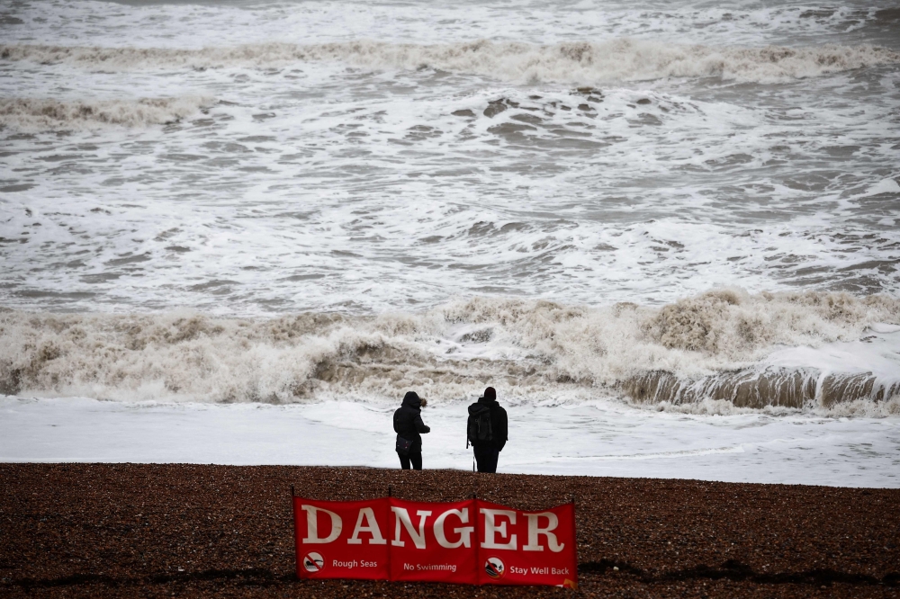 People look at the waves while standing behind a warning sign reading ‘Danger’ displayed on the beach in Brighton, southern England on January 1, 2025 as weather warnings were put in place for rain, snow and wind across the UK. — AFP pic