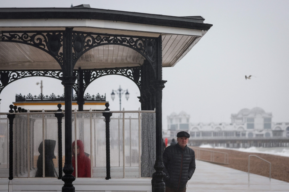 A man finds shelter from heavy rain on the South Parade Pier, in Portsmouth, southern England on January 1, 2025 as weather warnings were put in place for rain, snow and wind across the UK. — AFP pic