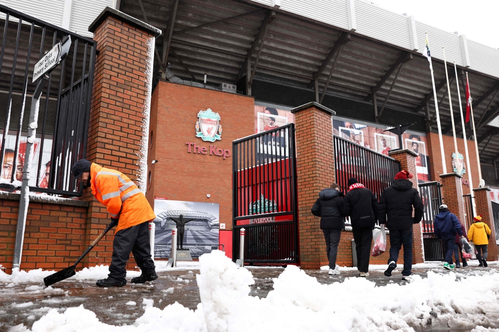 A member of staff cleans the pavement from the snow as supporters arrive ahead of the English Premier League football match between Liverpool and Manchester United at Anfield in Liverpool January 5, 2025. — AFP pic