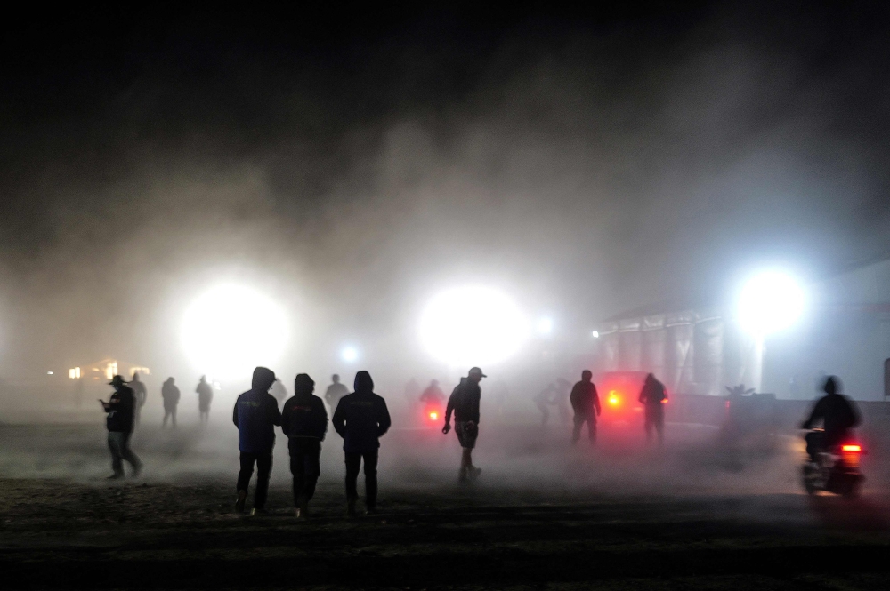 People walk in bivouac during the heavy rain, in Bisha on January 2, 2025, ahead of the start of the Dakar Rally 2025. — AFP pic