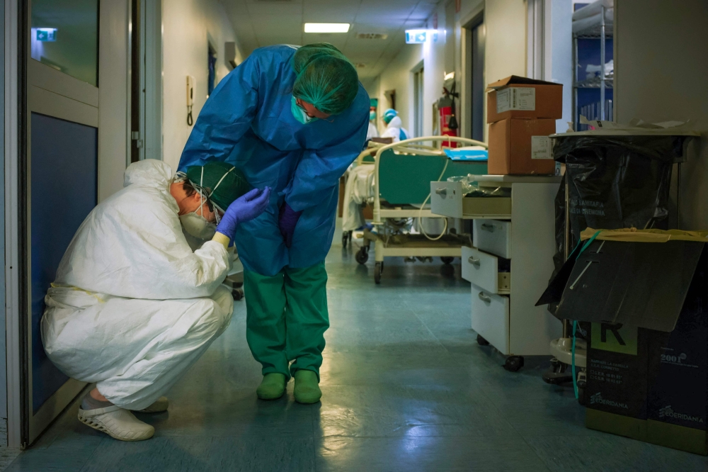 A nurse wearing protective mask and gear comforts another as they change shifts on March 13, 2020 at the Cremona hospital, southeast of Milan, Lombardy, during the country's lockdown aimed at stopping the spread of the Covid-19 pandemic. — AFP pic