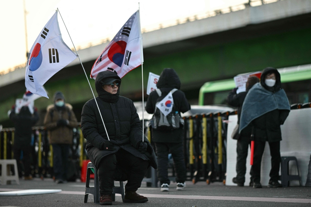 A supporter of impeached South Korean president Yoon Suk-yeol holds South Korean and US flags as commuters drive past a rally near Yoon’s residence in Seoul January 9, 2025. — AFP pic