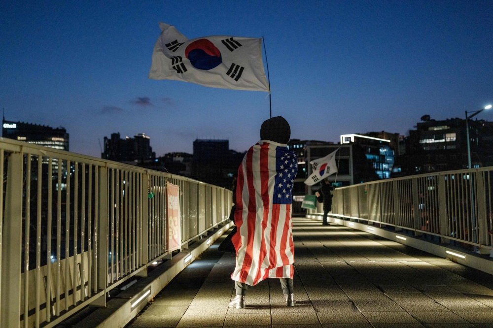 A supporter of impeached South Korean President Yoon Suk Yeol waves a South Korean flag as she wears a US flag on a pedestrian bridge near the President's residence in Seoul. — AFP