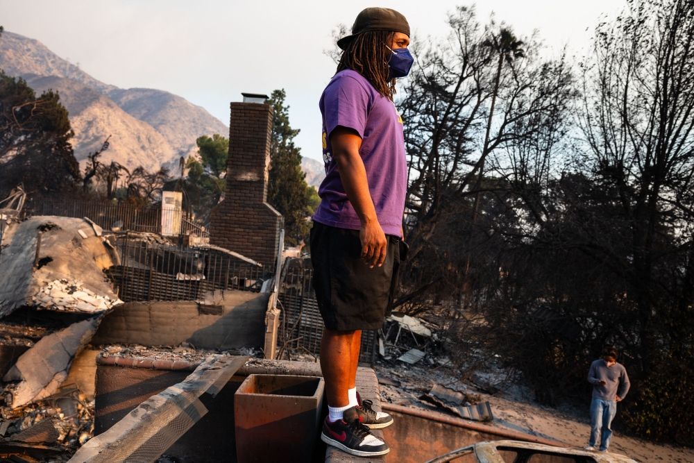 A young man looks out across the destruction from his family's home burned. — AFP