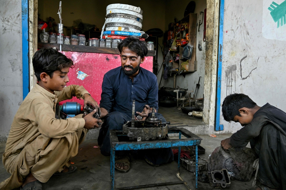 Kamran Imran (left), a 10-year-old schoolboy, works at a motorcycle workshop after finishing school in Abdullah Goth village on the outskirts of Karachi November 13, 2024. — AFP pic