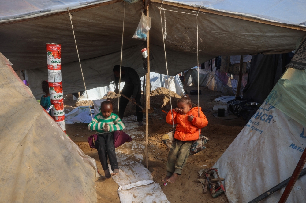 Palestinian girls sit on swings in their tent as their father Tayseer Obaid digs a trench in an attempt to protect his children from the cold and Israeli strikes, in a makeshift camp in Deir el-Balah January 8, 2025. — AFP pic