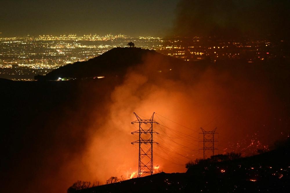 Flames and smoke are seen near power lines as the Palisades fire grows near the Mandeville Canyon neighborhood and Encino. — AFP