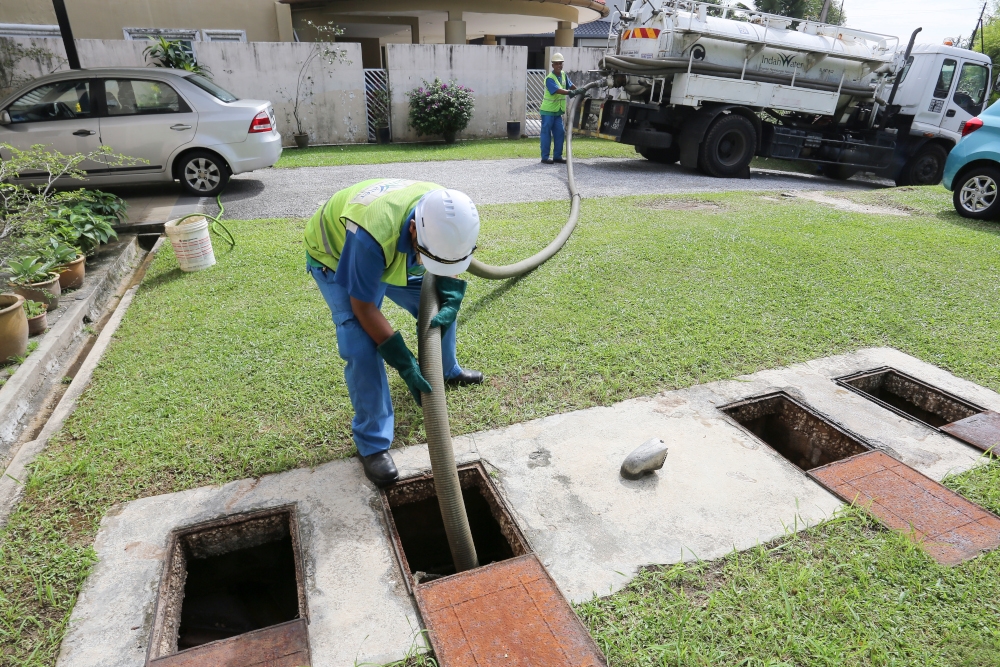 A pair of Indah Water Konsortium technicians desludge septic tanks in a residential area. — Picture courtesy of Indah Water Konsortium