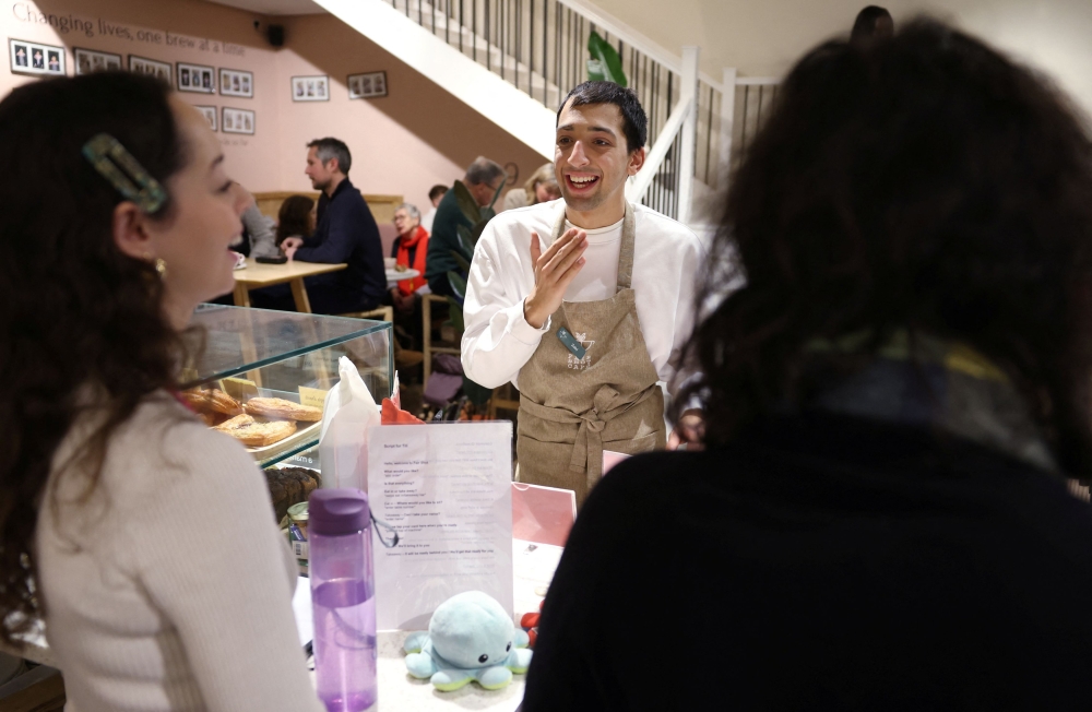 Zaki (centre) gets advice from skills coach Natalia, as they work in Fair Shot, a cafe set up to train young people with autism and other learning disabilities in employment skills, in central London, Britain, January 15, 2025. — Reuters pic