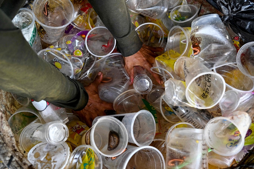 This photo taken on January 30, 2025 shows a worker pushing plastic drink glasses in a bag at a recycling depot on the outskirts of Phnom Penh. — AFP pic